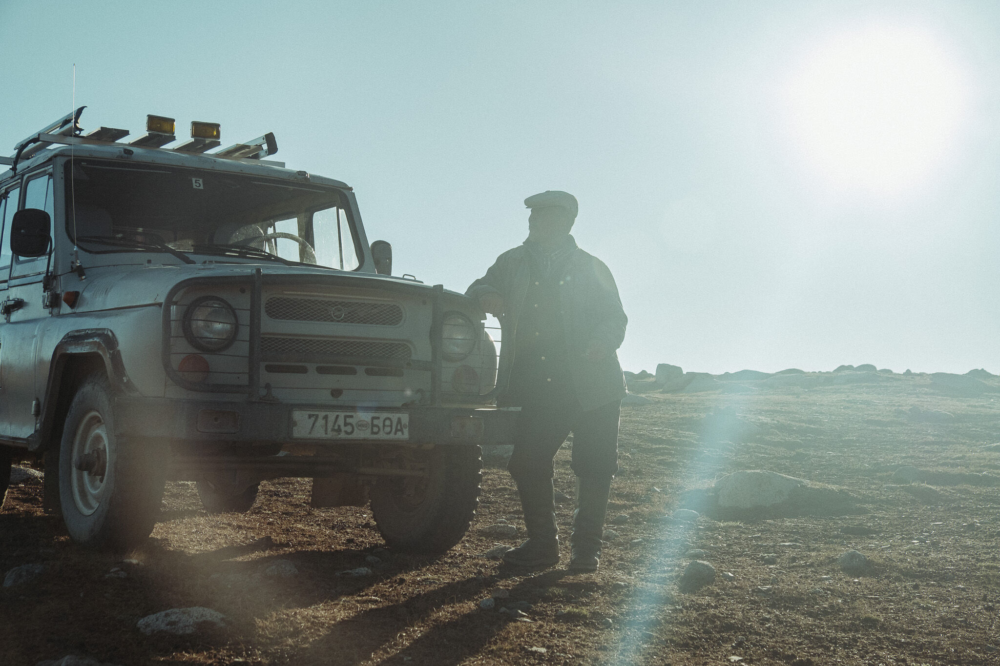 A herder and a jeep silhouetted against the low sun